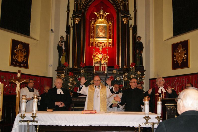 Biskup Marek Kamiński po lewicy kapłana katolickiego, a przed obrazem Maryi...
